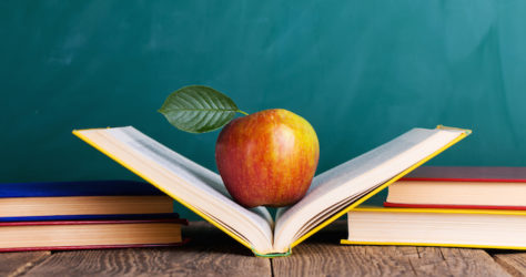 Still life with school books and apple against blackboard with "back to school" on background