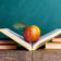 Still life with school books and apple against blackboard with "back to school" on background