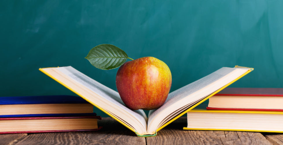 Still life with school books and apple against blackboard with "back to school" on background