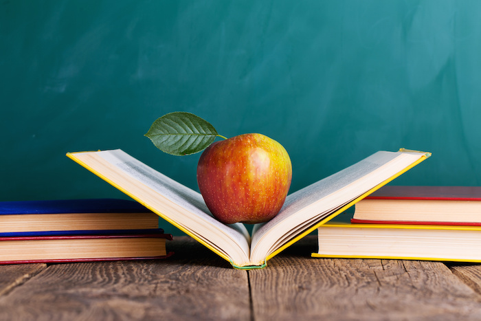 Still life with school books and apple against blackboard with "back to school" on background